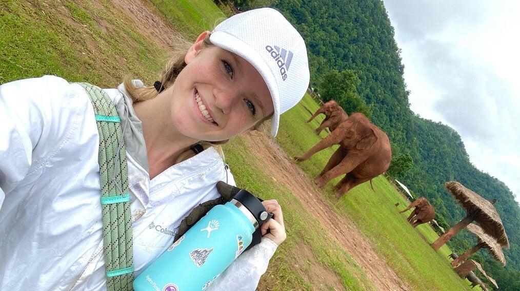 Renee D, Loop Abroad, College Veterinary Service Program alum Renee D wearing an Adidas white hat and braids smiling with elephants in the background